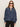 A woman in Sanctuary Clothing’s personal best blouse moonshadow—a loose, long-sleeve denim top with a gathered yoke and buttoned collar—pairs it with black pants, standing against a plain light background.
