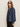 A woman with long, light brown hair models the Sanctuary Clothing personal best blouse moonshadow—black sunglasses, black pants, and a loose-fitting, dark denim top—standing against a plain light background.