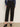 A person models the Sanctuary Clothing ponte barrel trouser in black, paired with a blue long-sleeve shirt and black heeled mules, standing against a plain light background. The waist-up photo excludes the person's face.