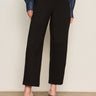 A person models the Sanctuary Clothing ponte barrel trouser in black, paired with a blue long-sleeve shirt and black heeled mules, standing against a plain light background. The waist-up photo excludes the person's face.