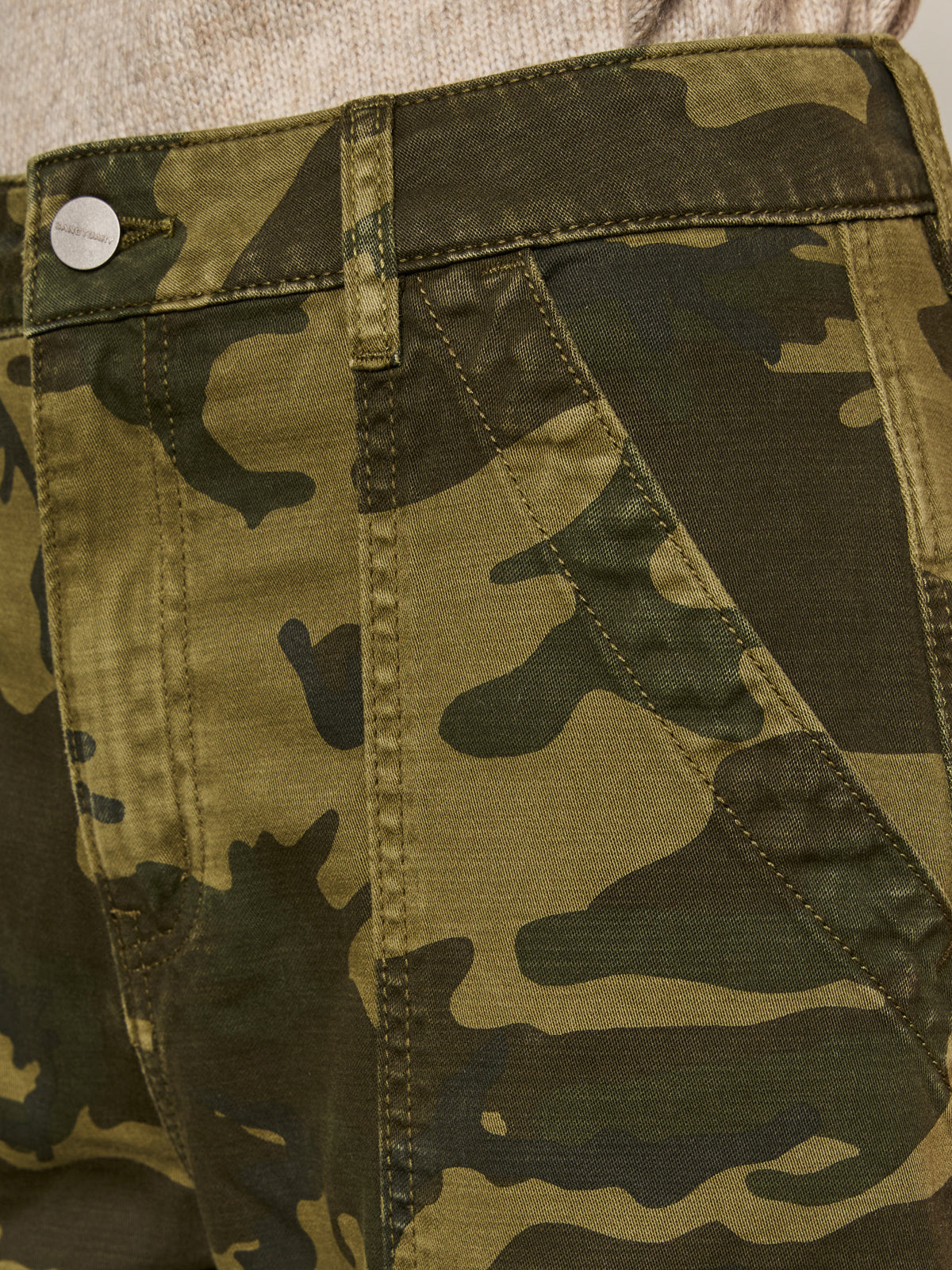 Close-up of Sanctuary Clothing's boyfriend utility pant in rambler camo, featuring green and brown camouflage, visible stitching, seam details, belt loops, front pockets, and a metal button at the waistband.