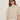 A woman with long brown hair wears black sunglasses, white pants, and the Sanctuary Clothing perfect sweater tee in heather pearl. She stands against a plain light background, looking slightly to the side with a neutral expression.