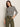 A woman poses against a light background wearing the Sanctuary Clothing boatneck long sleeve tee in light oat black stripe, paired with olive green cargo pants. She has a neutral expression and one hand in her pocket.