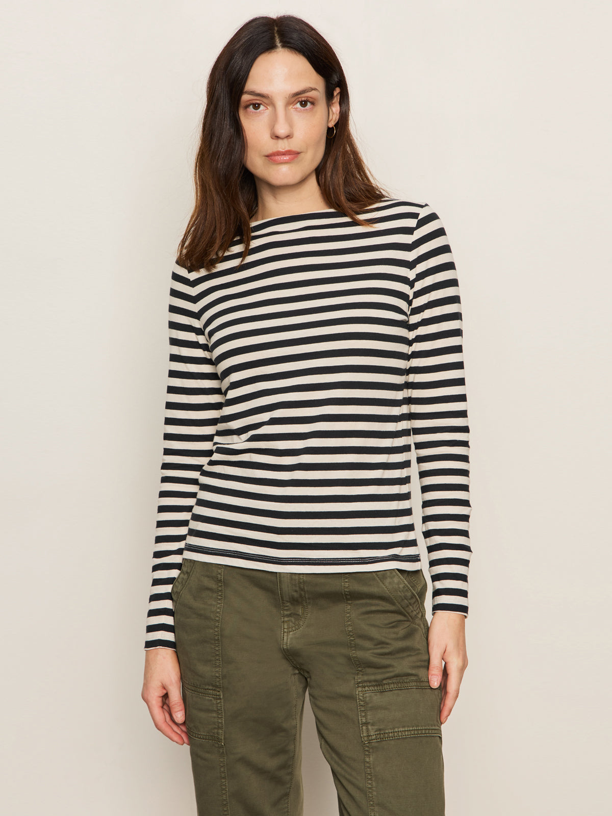 A woman with long brown hair wears the Sanctuary Clothing boatneck long sleeve tee in light oat black stripe, standing against a plain light background.