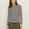 A woman with long brown hair wears the Sanctuary Clothing boatneck long sleeve tee in light oat black stripe, standing against a plain light background.
