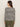 A woman with long brown hair, seen from behind, wears the Sanctuary Clothing boatneck long sleeve tee in light oat black stripe. She pairs it with olive green pants and stands against a plain light background.
