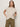A woman with long brown hair wears the Sanctuary Clothing draped sleeveless mock neck top in mother of pearl and olive-green pants, standing against a plain light background with her hands on her hips.