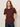 A woman with long, light brown hair wears the Sanctuary Clothing shirred waist dolman tee in chicory and dark blue jeans, standing against a plain light background with her hands in her pockets.