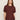 A woman with straight, light brown hair wears the Sanctuary Clothing Shirred Waist Dolman Tee in chicory and dark jeans, standing against a beige background and looking at the camera with a neutral expression.