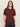 A woman with straight, light brown hair wears the Sanctuary Clothing Shirred Waist Dolman Tee in chicory and dark jeans, standing against a beige background and looking at the camera with a neutral expression.