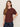 A woman with long brown hair stands against a light background, wearing the Sanctuary Clothing shirred waist dolman tee in chicory, and dark blue jeans, looking at the camera with a neutral expression.