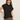 A woman poses confidently with one hand on her hip against a plain light background, wearing black sunglasses, leopard print pants, and the Sanctuary Clothing draped sleeveless mock neck top in black.