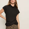 A woman poses confidently with one hand on her hip against a plain light background, wearing black sunglasses, leopard print pants, and the Sanctuary Clothing draped sleeveless mock neck top in black.
