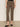 A person wears Sanctuary Clothing's Carnaby Kick Crop Leggings in French Kitty print, paired with a black top, black slip-on shoes, and a gold bangle, standing relaxed against a beige wall.