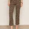 A person wears Sanctuary Clothing's Carnaby Kick Crop Leggings in French Kitty print, paired with a black top, black slip-on shoes, and a gold bangle, standing relaxed against a beige wall.
