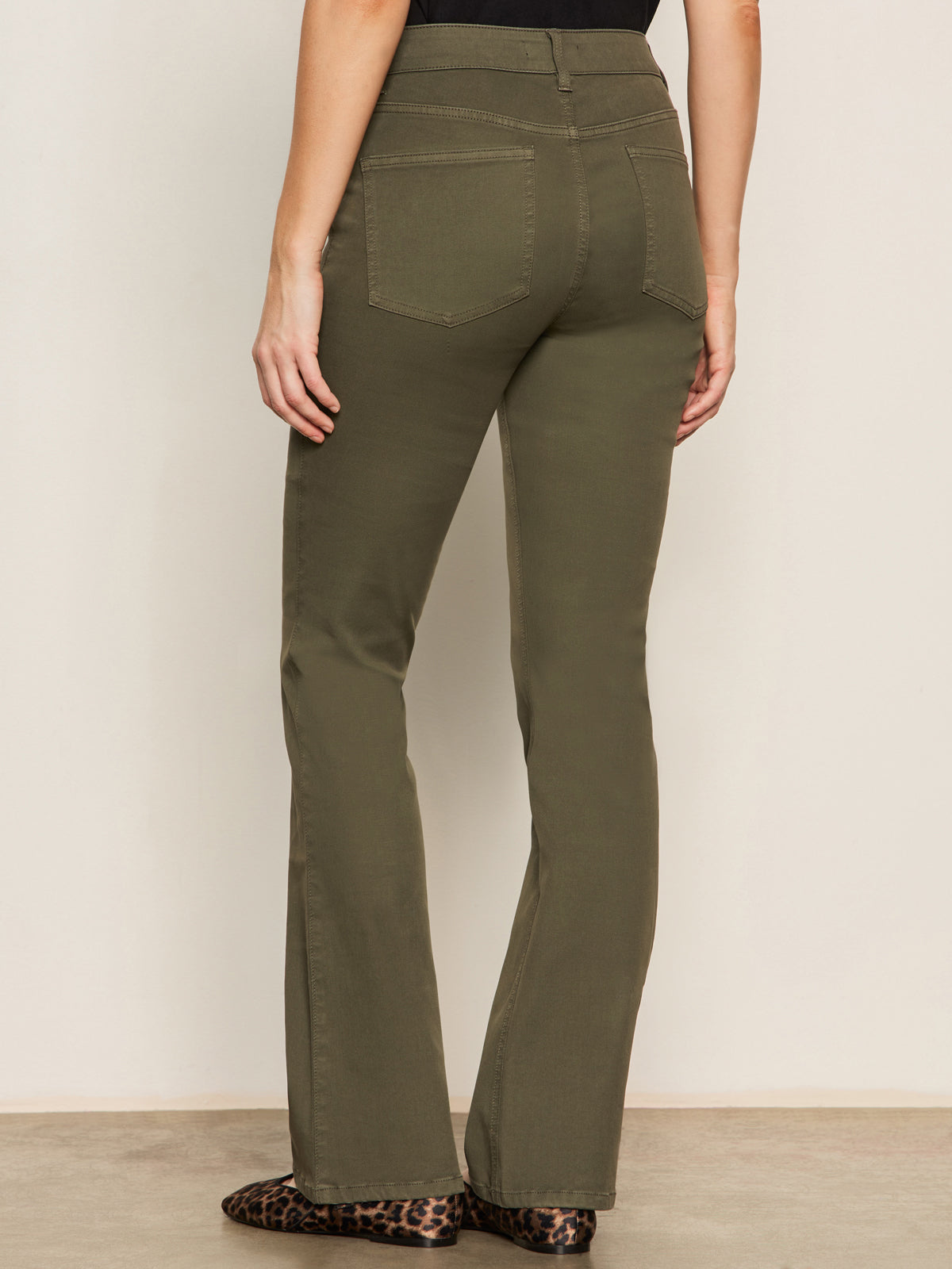 Someone is standing with their back to the camera against a neutral background, wearing Sanctuary Clothing's sculpted brook bootcut pant in kalamata and leopard print flats.