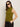 A woman wears the Sanctuary Clothing fuzzy shell martini olive sleeveless turtleneck sweater, paired with black pants and large black sunglasses, standing against a neutral background with one hand in her pocket.