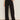 A person indoors wears Sanctuary Clothing's modern gab trouser black with a green top and black pointed-toe shoes, one hand in their pocket. Their head is not visible in the image.