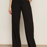 A person indoors wears Sanctuary Clothing's modern gab trouser black with a green top and black pointed-toe shoes, one hand in their pocket. Their head is not visible in the image.