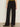 A person wearing Sanctuary Clothing’s modern gab trouser black with black pointed-toe shoes stands against a plain light-colored wall; only the lower half of the body is visible.