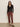 A woman wearing sunglasses, a black long-sleeve buttoned top, Sanctuary Clothing cadence 90s straight crop jeans in chicory, and leopard-print shoes stands against a plain light-colored wall.