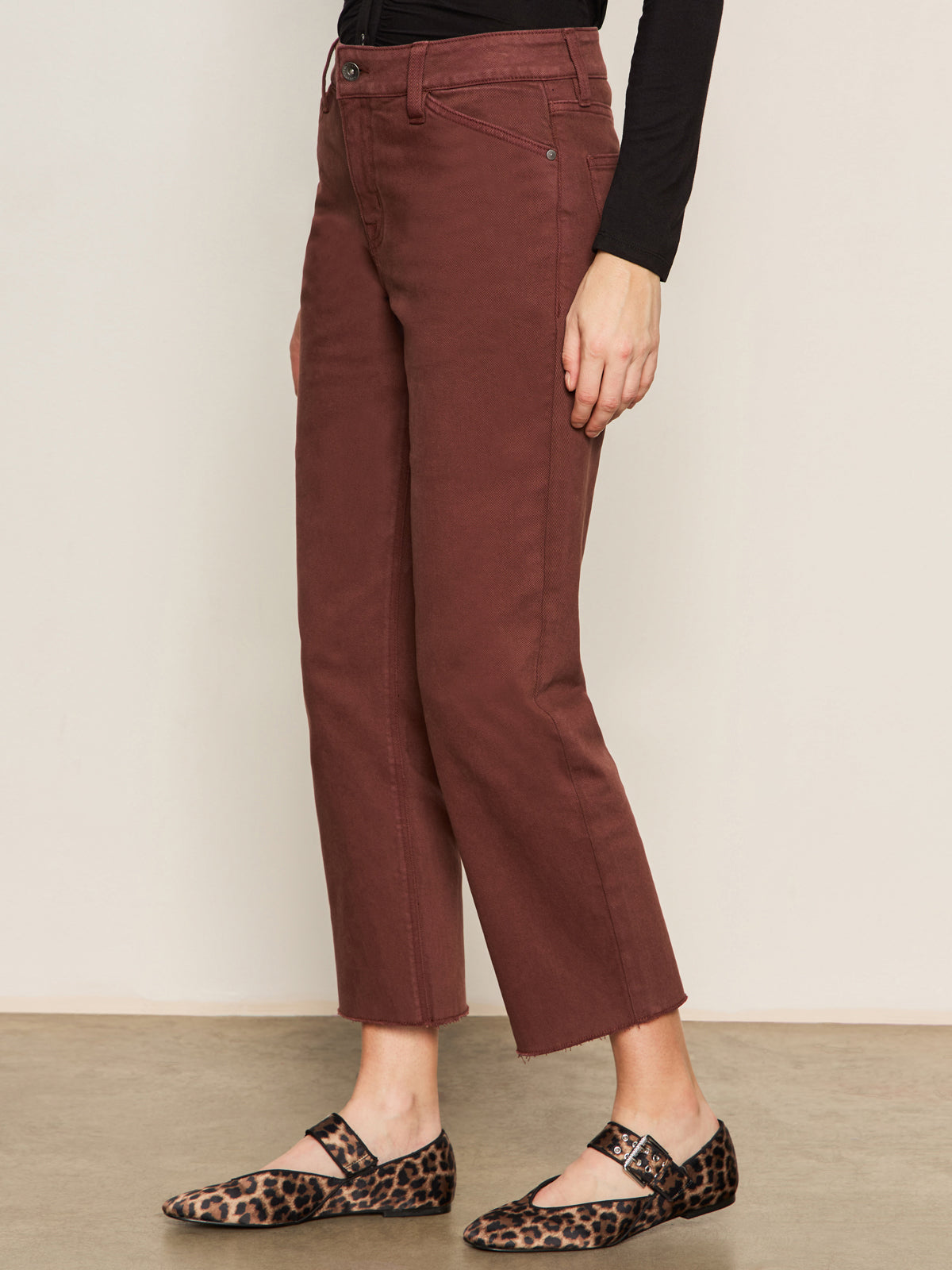 A person wears Sanctuary Clothing's cadence 90s straight crop jeans in chicory, paired with a black long-sleeve top and leopard-print Mary Jane flats, standing against a neutral background.