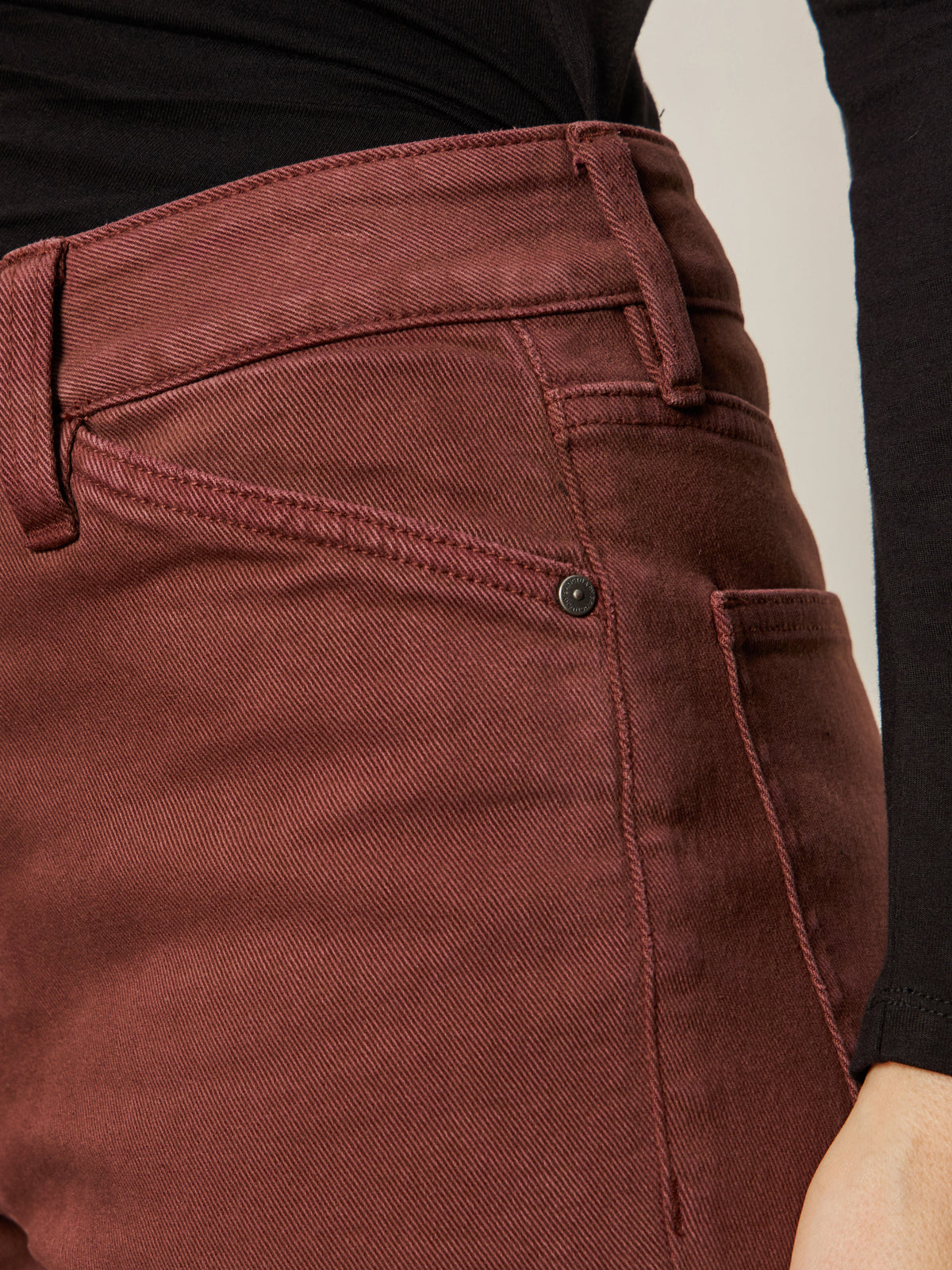 Close-up of a person wearing Sanctuary Clothing's Cadence 90s Straight Crop Jeans in chicory, showcasing the high waist, pocket detail, seams, and belt loops paired with a black long-sleeve top.