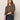 A woman with long brown hair wears the Sanctuary Clothing 24 7 popover french kitty sweater, tucked into high-waisted dark blue jeans, posing against a plain light background.