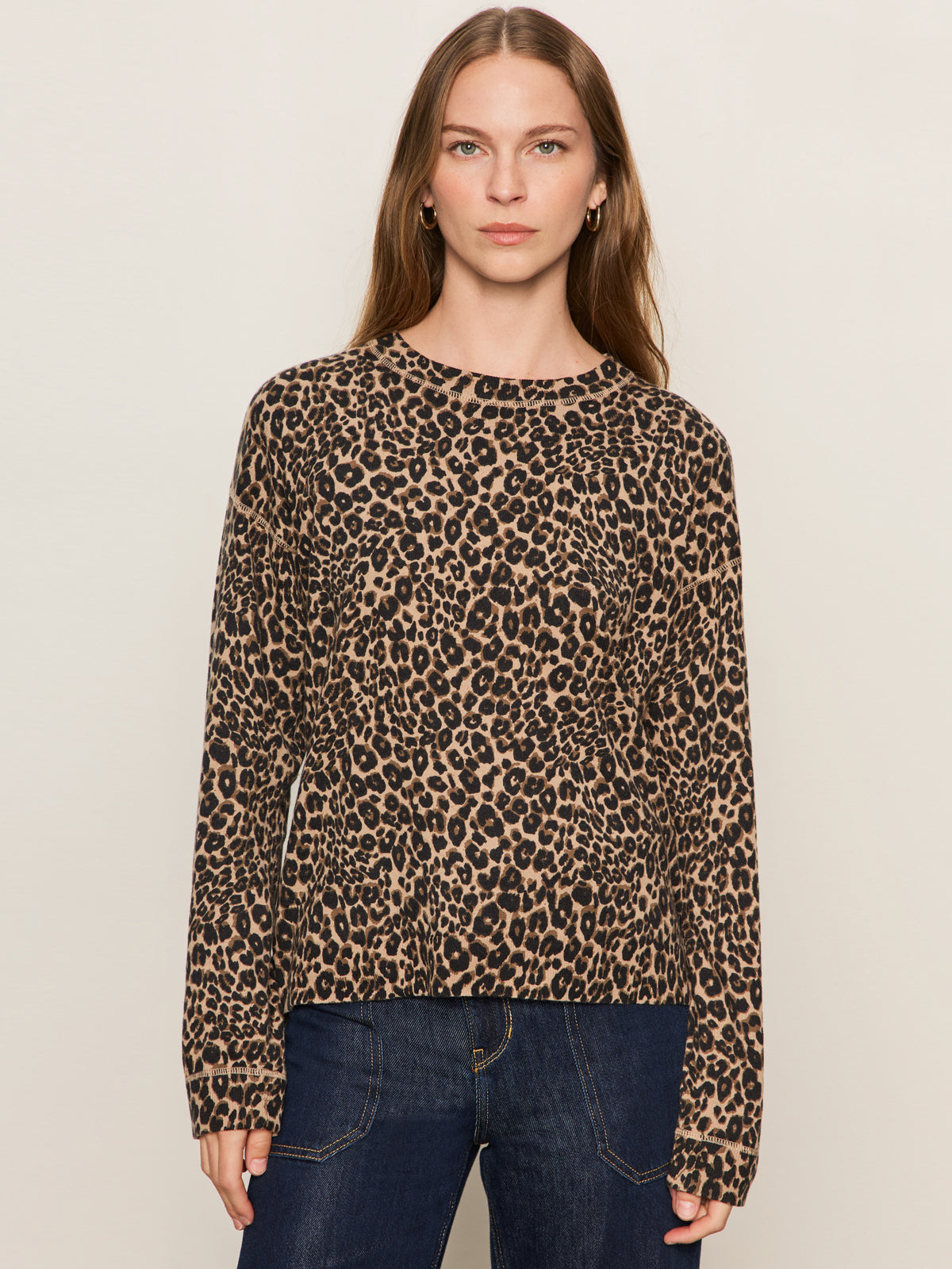 A woman with long brown hair models the Sanctuary Clothing 24/7 Popover French Kitty, a long-sleeve brown and black leopard print sweater, paired with dark blue jeans against a plain light background.