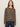 A woman with long brown hair models the Sanctuary Clothing 24/7 Popover French Kitty, a long-sleeve brown and black leopard print sweater, paired with dark blue jeans against a plain light background.