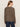 A woman with long brown hair is seen from behind, wearing the Sanctuary Clothing 24 7 Popover French Kitty top and dark blue jeans, standing against a plain light-colored background.