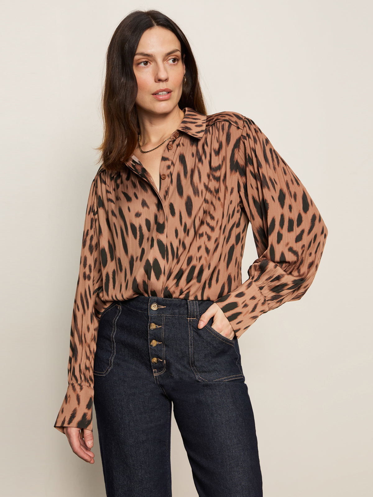 A woman with straight brown hair and a neutral expression wears the Sanctuary Clothing 'colette shirt mocha leo', an animal print blouse with long sleeves, paired with high-waisted dark blue jeans featuring visible buttons.
