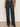 A person wears Sanctuary Clothing’s ekara slim wide jean in indigo dark rinse wash, featuring prominent seams and front buttons, paired with an animal print long-sleeve blouse and black shoes against a plain background.