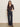 A woman stands against a plain light wall, wearing the Sanctuary Clothing textured knit dreamgirl top semi sweet with high-waisted dark blue wide-leg jeans and brown heeled shoes.