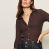 A woman with long brown hair models the Sanctuary Clothing Textured Knit Dreamgirl Top in Semi Sweet, a dark brown collared button-up, paired with high-waisted jeans. She poses with one hand on her hip against a plain background.