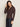 A woman with long brown hair wears the Sanctuary Clothing textured knit dreamgirl top semi sweet, a brown button-up with long sleeves, and dark high-waisted jeans. She stands against a light beige background, looking down and touching her hair.