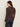 A woman with long brown hair faces away, wearing the Sanctuary Clothing textured knit Dreamgirl Top in Semi Sweet and dark jeans against a plain light background.