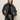 Wearing the Sanctuary Clothing boyfriend trucker jacket in washed black denim, a person stands against a plain light background with hands in pockets, paired with a leopard print collar, black knit sweater, and black leather pants.