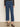 A person wearing Sanctuary Clothing's the marine jeans aspen—high-waisted, cropped blue jeans with front patch pockets—paired with a sheer black long-sleeve top and brown leopard-print flats stands against a neutral background.