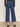 A person wears Sanctuary Clothing's The Marine Jeans Aspen—high-waisted, wide-leg blue jeans with back pockets—paired with a sheer black long-sleeve top and leopard-print flats, standing on a neutral floor facing away.
