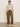 A woman stands against a plain wall wearing Sanctuary Clothing’s boyfriend utility pant in kalamata, a beige short-sleeve sweater, and light woven slip-on shoes. Her hair is pulled back and her hands are relaxed at her sides.