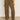 A person wearing Sanctuary Clothing’s boyfriend utility pant kalamata and a light beige top with white woven flats stands on a polished concrete floor against a plain light-colored wall.