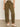 A person wearing Sanctuary Clothing’s boyfriend utility pant kalamata and a light beige top with white woven flats stands on a polished concrete floor against a plain light-colored wall.