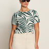 A woman wearing Sanctuary Clothing's the perfect tee green oasis (extended sizing) and high-waisted cream pants stands against a light background, with one hand in her pocket.