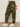 A person stands indoors in Sanctuary Clothing boyfriend utility pant rambler camo (extended sizing), a white textured long-sleeve top, and white Adidas sneakers. The side view photo captures them from shoulders to feet.