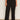 A person wears Sanctuary Clothing's runway ponte trouser in black extended sizing and white sneakers, standing against a plain light-colored wall with their arms relaxed at their sides.