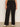 A person wears Sanctuary Clothing's runway ponte trouser in black extended sizing and white sneakers, standing against a plain light-colored wall with their arms relaxed at their sides.