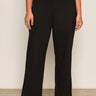 A person wears Sanctuary Clothing's runway ponte trouser in black extended sizing and white sneakers, standing against a plain light-colored wall with their arms relaxed at their sides.