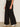 A person in Sanctuary Clothing's runway ponte trouser black (extended sizing), paired with white sneakers featuring a black stripe and a camo-patterned top, poses indoors against a neutral background.