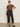 A woman wears Sanctuary Clothing's the marine jeans after hours extended sizing with sunglasses, a brown patterned short-sleeve top, and black flats, standing against a plain light wall with one hand on her hip.